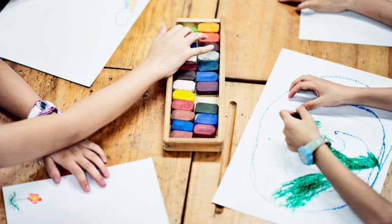 hands of kids using chalk to draw