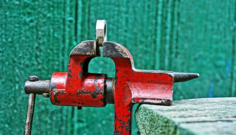 A red vice grips a metal bolt against a green wall
