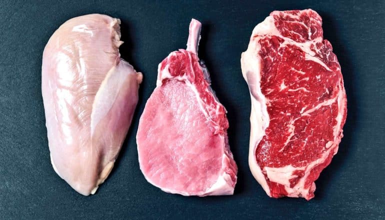 raw chicken breast, pork chop, and steak on stone surface
