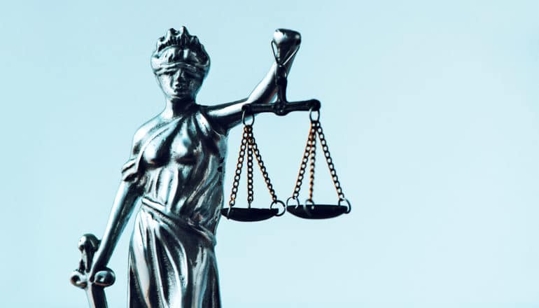 A metal statue of Lady Justice holds scales against a light blue background