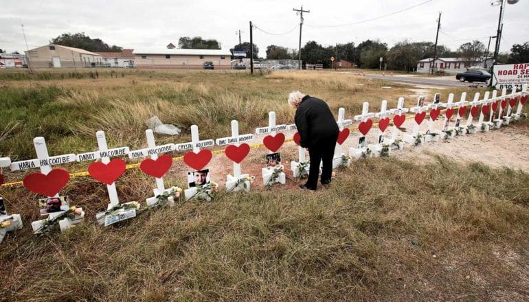 person stands before long line of crosses with hearts and photos attached to each