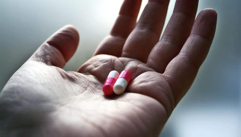 A person holds two pink and white pills in the palm of their hand