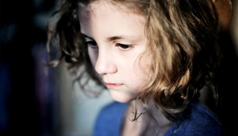 A young girl looks downward in sadness or deep thought with some of her face covered in shadow