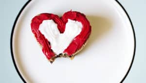 A heart-shaped donut sitting on a white and blue plate has one bite taken out of it