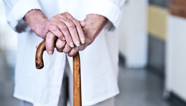 An older woman leans on her wooden cane with both hands