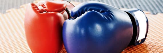 Two boxing gloves sit on a gym floor, one blue and one red