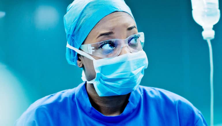 A doctor with face mask and goggles on looks to her left while in the operating room