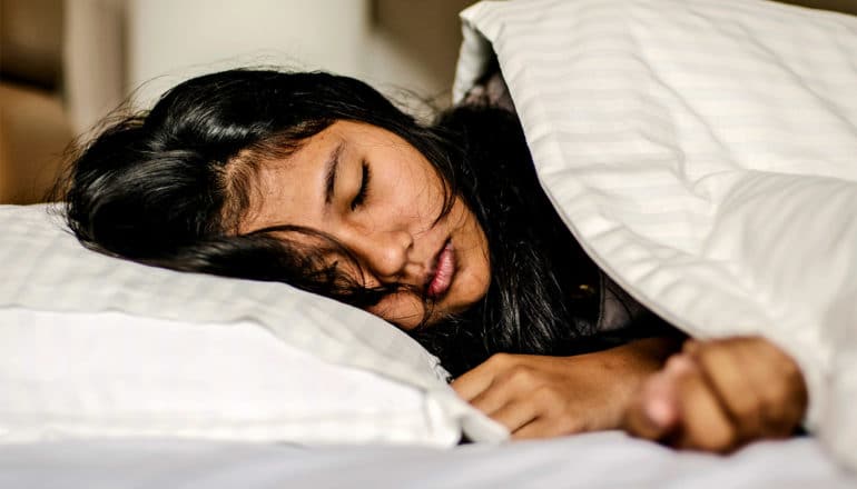 A teen girl sleeps on her side in bed