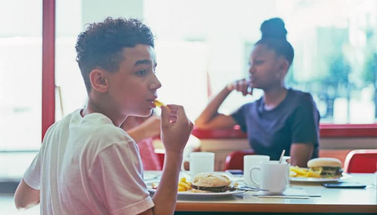 worried teen boy eating fast food across table from teen girl