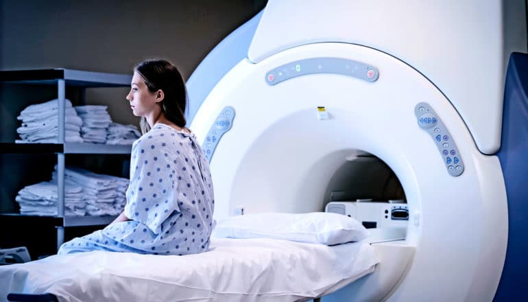 A girl is sitting on an MRI examination table in a hospital gown