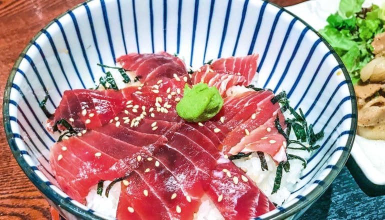 A white and blue striped bowl of rice with fish and wasabi on top