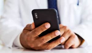 A doctor holds a black iPhone while sitting at a desk