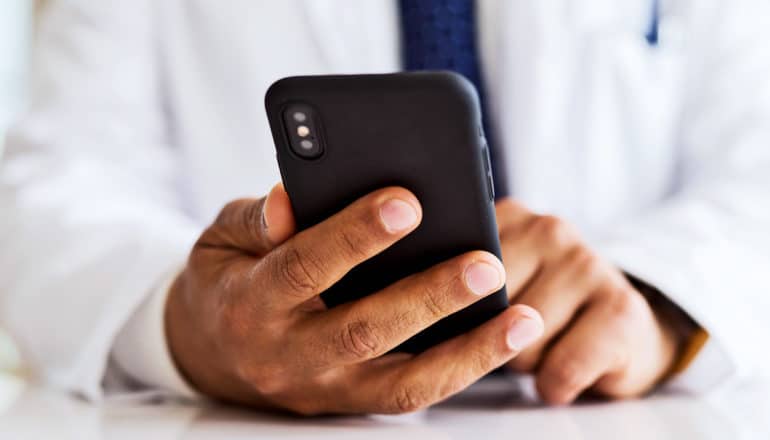 A doctor holds a black iPhone while sitting at a desk