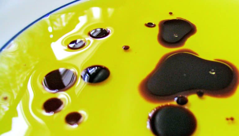 A plate with oil and vinegar, with the vinegar forming droplets within the oil