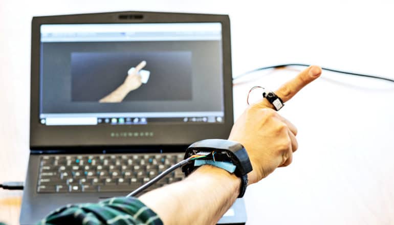 A researcher wearing the AuraRing system shows off the hand and finger tracking, with his hand showing up on a computer screen