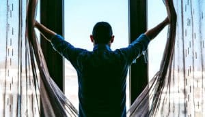 A man flings open curtains and looks outside his window