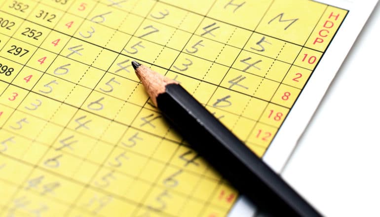 A yellow golf scorecard sits on a white background with a black pencil on top of it