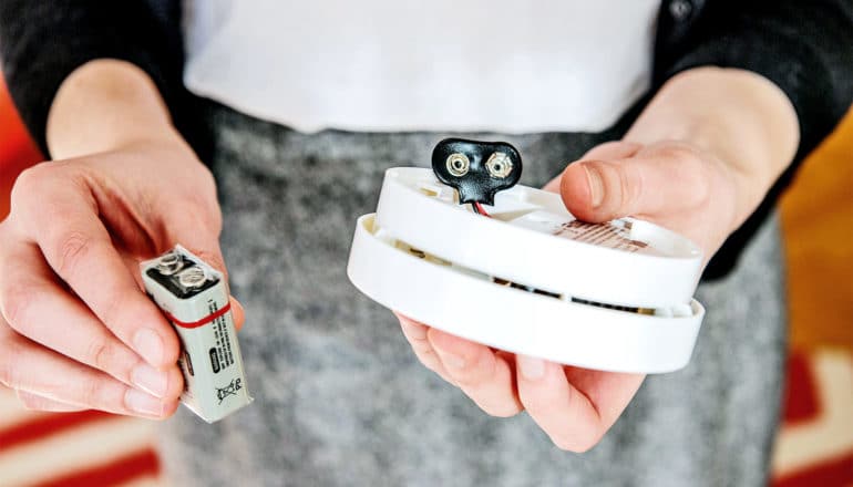 A woman holds a carbon monoxide detector and its battery