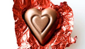 heart-shaped chocolate sits on open, red shiny wrapper