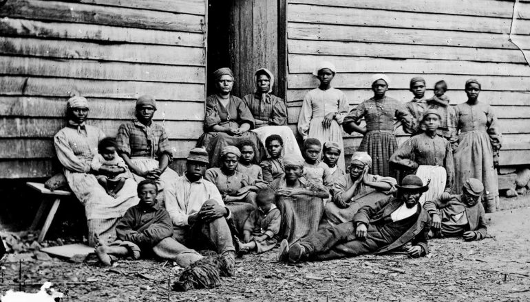 A group of refugees are bunched for a picture in front of a wooden house