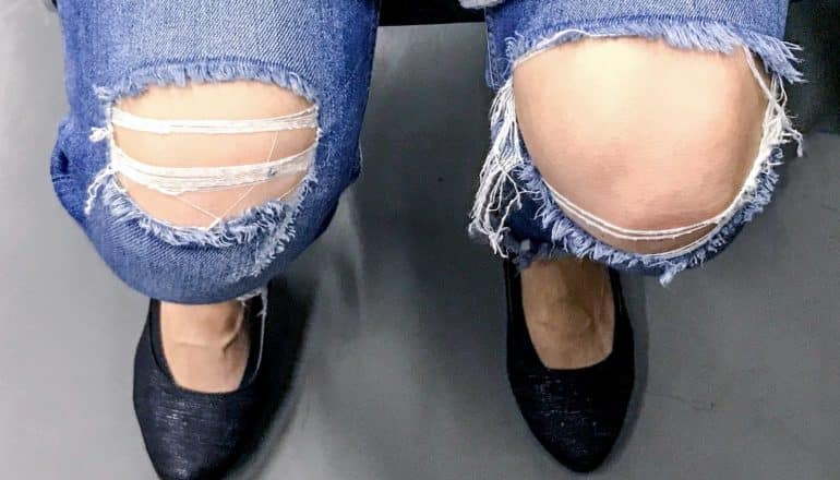 knees and feet of seated person wearing ripped jeans