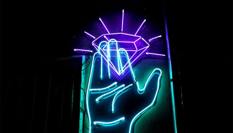 A blue and purple neon sign shows a hand holding a shining diamond