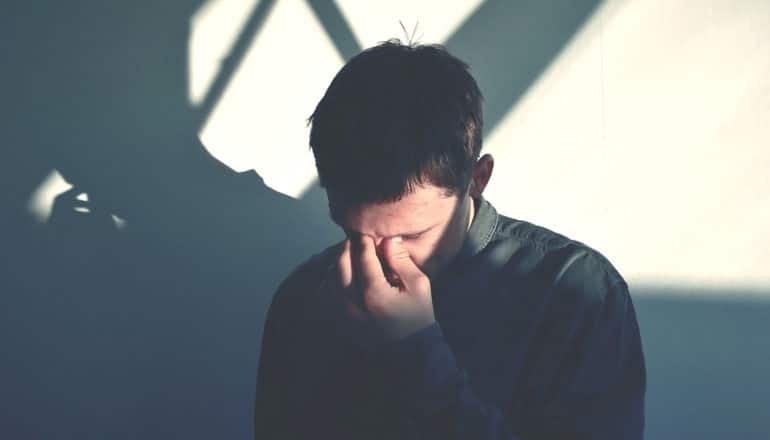 shadows fall across face of man with hand to his face