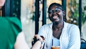 A young woman shakes a job interviewers hand as they meet outside at a coffee shop