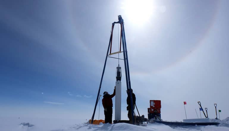 lens flare behind researchers using equipment to pull ice core from the ground