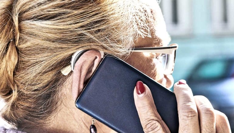 An older woman speaks on the phone while using a hearing aid