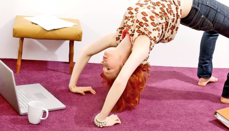 person does reverse bend yoga move whiel looking at laptop with cup of coffee