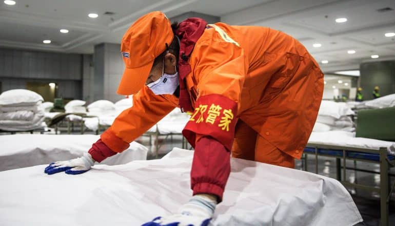 person in uniform, mask, and gloves bends over hospital bed