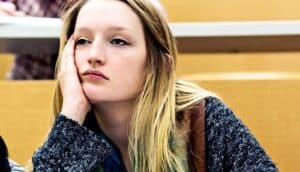 A young woman rests her face on her hand, bored in a lecture hall