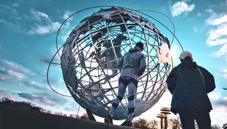 Two people look up at a large metal globe that has a few rings around it