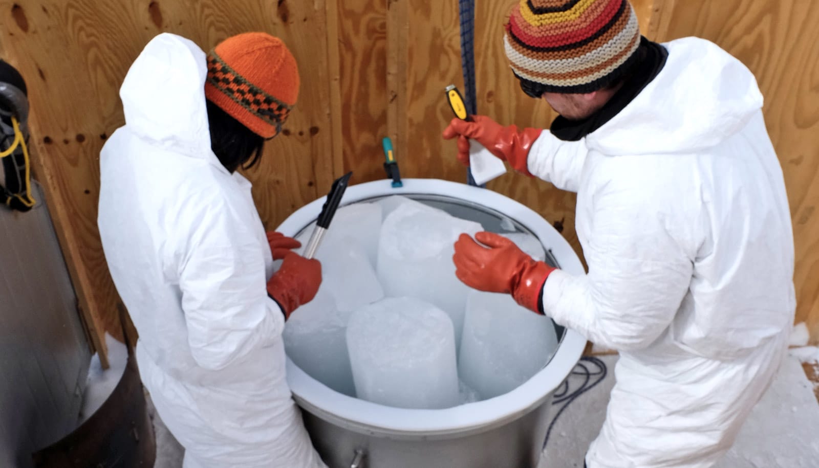 two researchers in white suits handle ice cores in large container