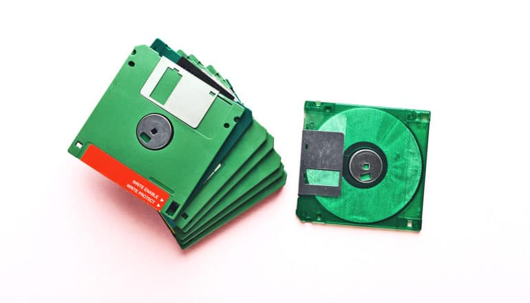 A stack of green floppy disks sit on a white background, with one off to the side
