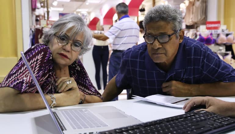 two people lean to look at laptop