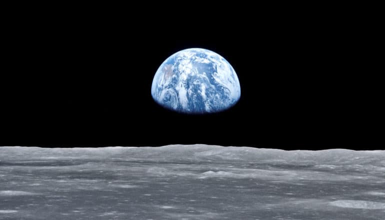 Earth rises over the surface of the moon, blue against the black background of space