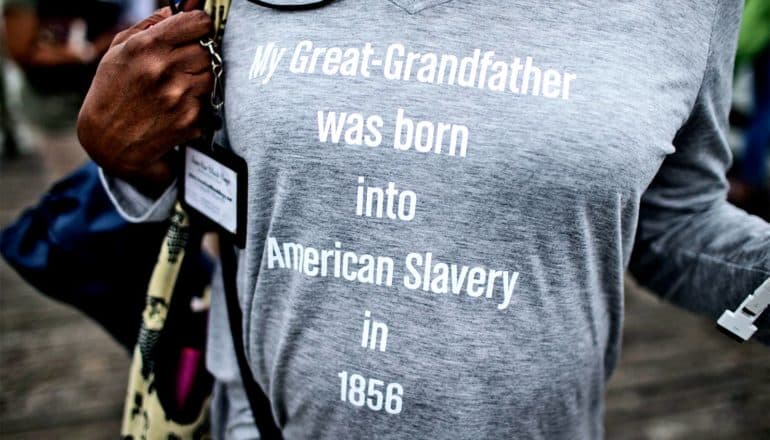 A woman wears a t-shirt that reads, "My Great-Grandfather was born into American Slavery in 1856"