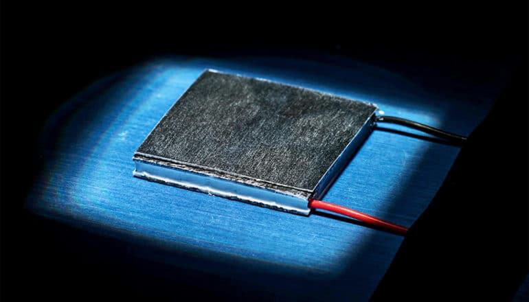 A small piece of black metal sits on a blue surface with a black and a red wire coming out of the bottom