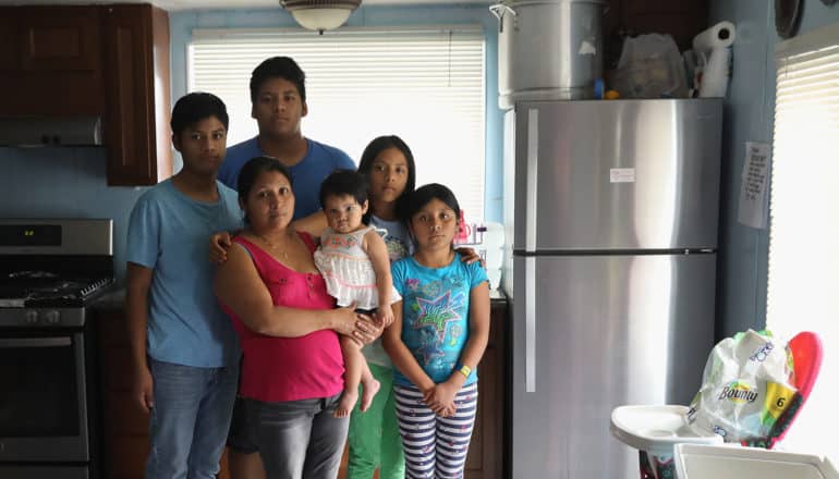 family of six, standing and serious, pose in kitchen