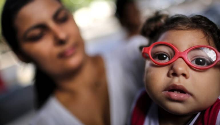 baby's face in foreground with red glasses; adult in background