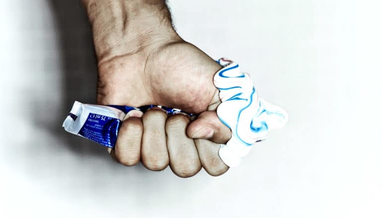 A person squeezes toothpaste out of a tube all over their hand