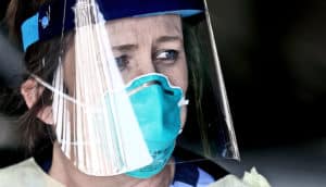 Canova wears a blue face mask and clear protective face shield looks concerned