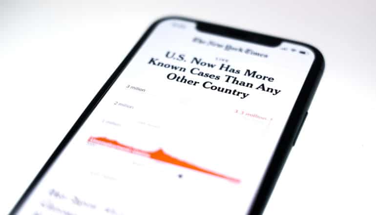 NYT headline on phone: "US now has more known cases than any other country" above blurred graph