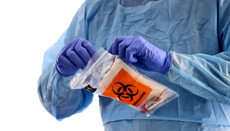 person in protective gear and gloves holds biohazard bag