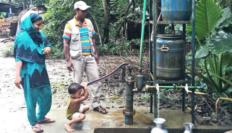 A young child uses pumps water while his mother and father look on