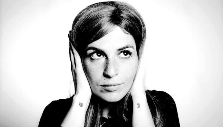 A young woman covers her ears and looks up and to her left