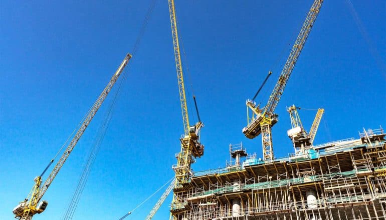 Yellow cranes against a blue sky work on a building under construction