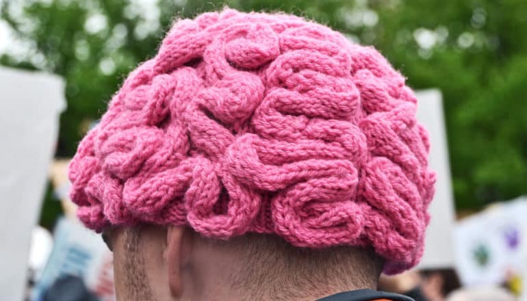 A man wears a pink knitted cap that looks like a brain